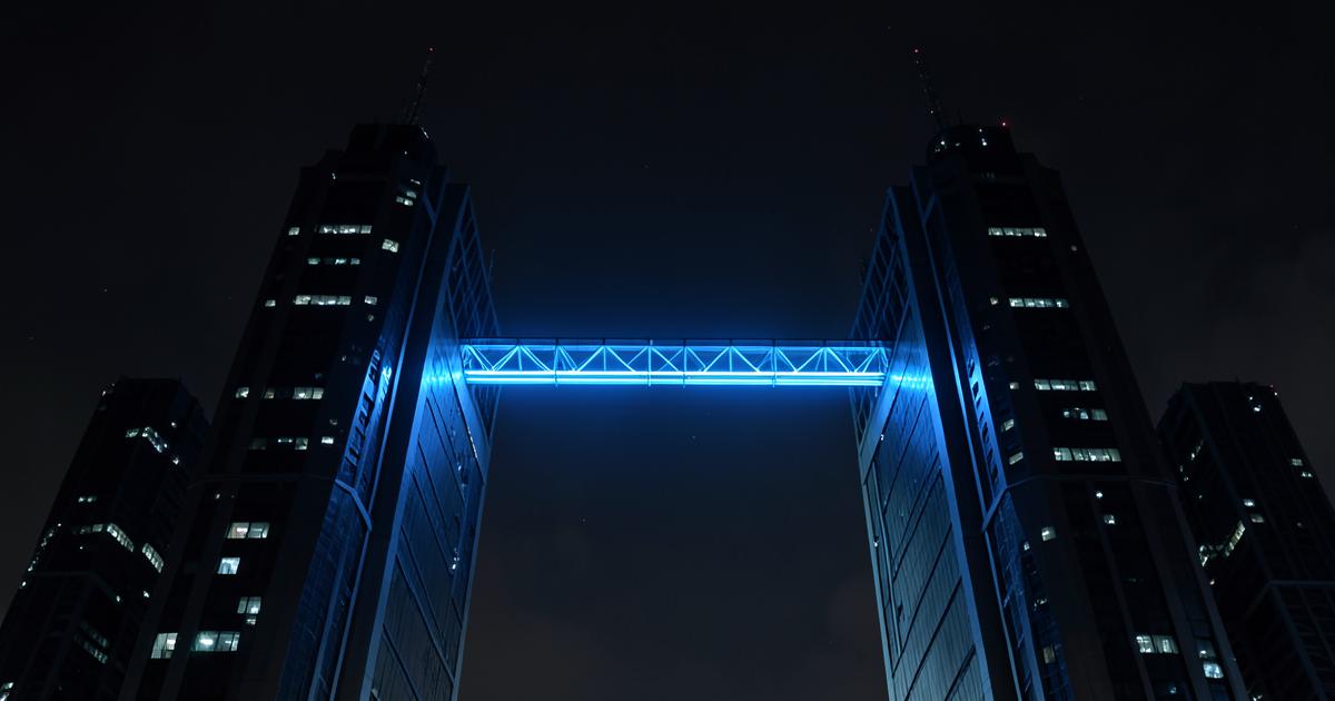 Blue glowing bridge between two dark towers at night